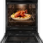 Foto frontal do fogão 4 bocas Continental branco automático com mesa compartimentada, modelo FC4CB – bivolt com a porta do forno aberta. Dentro dele, há uma luz interna na parte de cima e um frango assado com batatas em um refratário de vidro que está em cima de uma prateleira feita de grades, ela é removível e regulável em três alturas diferentes.