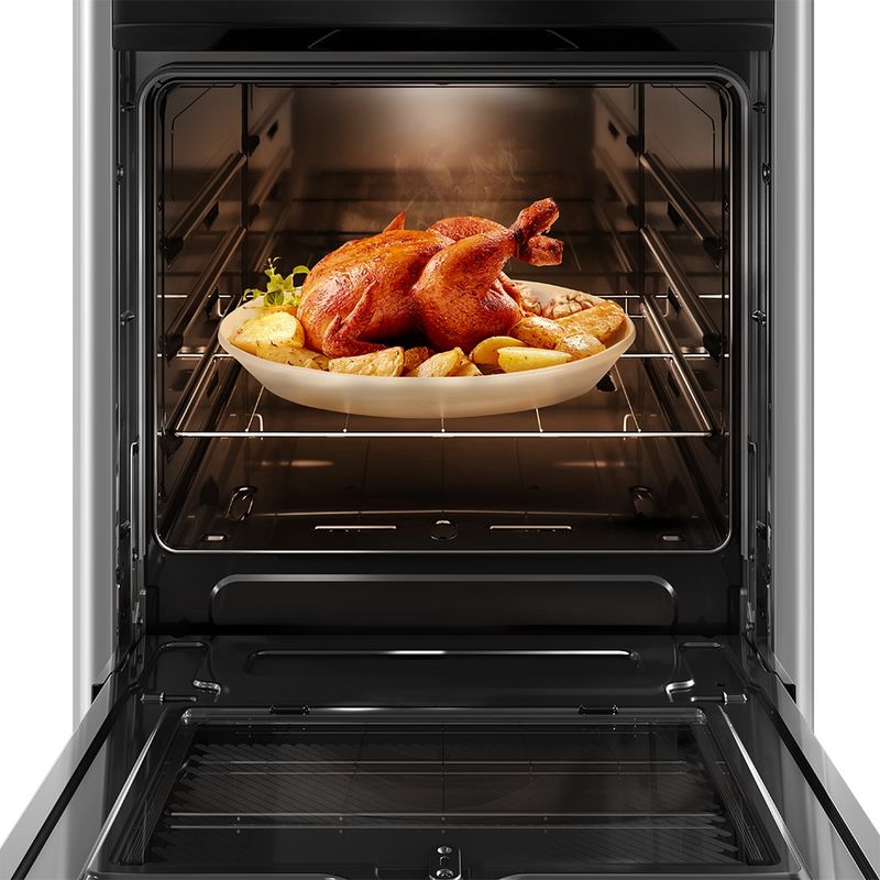 Foto frontal do fogão 4 bocas Continental prata automático com mesa compartimentada, modelo FC4CS- bivolt com a porta do forno aberta. Dentro dele, há luz interna na parte de cima e um frango assado com batatas em um refratário de vidro que está em cima de uma prateleira feita de grades, ela é removível e regulável em três alturas diferentes.