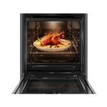 Foto frontal do fogão 4 bocas Continental automático preto com mesa de vidro temperado, modelo FC4VP – bivolt com a porta do forno aberta. Dentro dele, há um frango assado com batatas em um refratário de vidro que está em cima de uma prateleira feita de grades, ela é removível e regulável em três alturas diferentes.