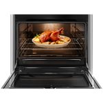Foto frontal do fogão 5 bocas continental automático prata com mesa de vidro temperado, modelo FC5VS - bivolt com a porta do forno aberta. Dentro dele, há luz interna na parte de cima e um frango assado com batatas em um refratário de vidro que está em cima de uma prateleira feita de grades, ela é removível e regulável em três alturas diferentes.