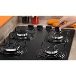 Foto-em-close-de-mao-mexendo-em-um-dos-botoes-do-cooktop-4-bocas-continental-a-gas-de-vidro-temperado-preto-modelo-KC4GP---bivolt-instalado-em-uma-bancada-com-marmore-bege.-Em-destaque-aparecem-algumas-bocas-queimadores-e-suas-grades-individuais.