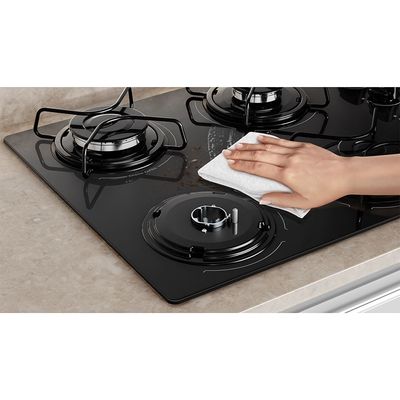 Foto-em-close-de-mao-limpando-com-um-pano-macio-o-cooktop-4-bocas-continental-a-gas-de-vidro-temperado-preto-modelo-KC4GP---bivolt-instalado-em-uma-bancada-com-marmore-bege.-Em-destaque-aparece-uma-das-bocas-sem-o-queimador-nem-a-grade-individual.