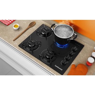 Foto-tirada-de-cima-pra-baixo-levemente-na-diagonal-do-cooktop-4-bocas-continental-a-gas-de-vidro-temperado-preto-modelo-KC4GP---bivolt-instalado-em-uma-bancada-com-marmore-bege.-Sao-2-bocas-na-lateral-esquerda-e-2-na-lateral-direita-todas-com-grades-individuais.-A-direta-ficam-os-botoes-dos-queimadores.-Ha-uma-panela-com-agua-fervendo-em-1-das-bocas-e-utensilios-de-cozinha-ao-redor-do-produto-como-colher-de-pau-potes-de-tempero-e-luva-termica-para-forno-e-fogao.