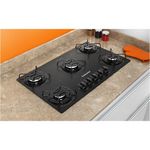 Foto-tirada-de-cima-pra-baixo-levemente-na-diagonal-do-cooktop-5-bocas-Continental-a-gas-de-vidro-temperado-preto-modelo-KC5GP-–-bivolt-instalado-em-uma-bancada-com-marmore-bege.-Sao-2-bocas-na-lateral-esquerda-uma-maior-no-meio-e-2-na-lateral-direita.-Todas-elas-com-grades-individuais.-Na-parte-da-frente-da-boca-do-meio-ficam-os-botoes-dos-queimadores.-Ha-utensilios-de-cozinha-ao-redor-do-produto-como-luva-termica-para-forno-e-fogao-e-potes-de-tempero.