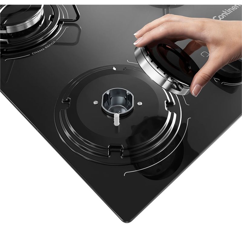 Foto em close de mão segurando o queimador de umas das bocas do cooktop 5 bocas Continental a gás de vidro temperado preto, modelo KC5GP.